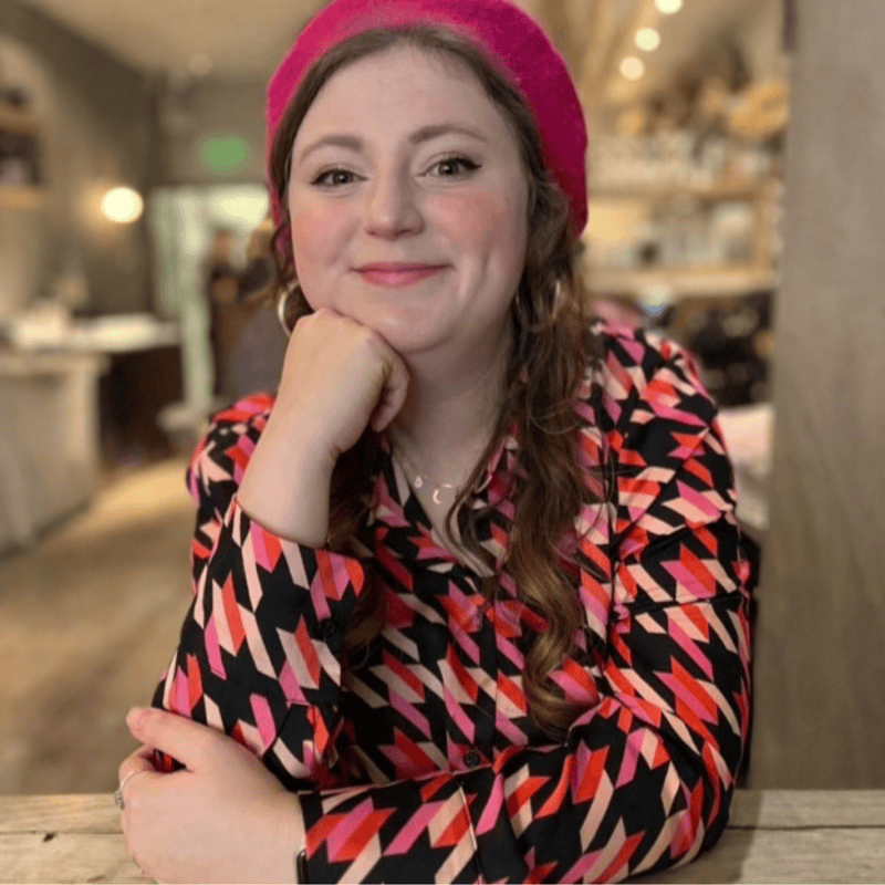 Woman smiling at Sunrise Film Festival, wearing a pink hat and patterned top.
